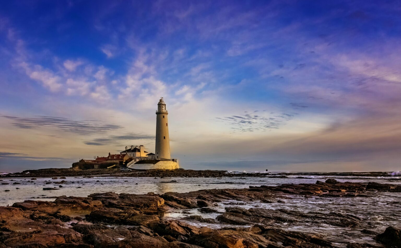 Lighthouse overlooking the rocky seashore at dusk, under a vibrant sky.